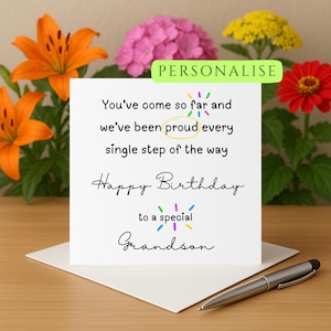 Puede incluir: Una tarjeta de felicitación blanca con el texto "You've come so far and we've been proud every single step of the way Happy Birthday to a special Grandson". La tarjeta está sobre un sobre blanco con un bolígrafo plateado. Flores en el fondo.