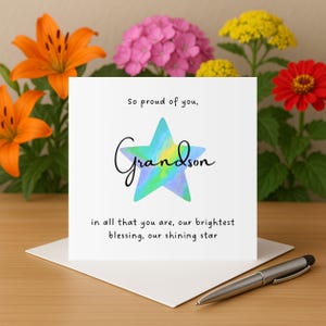 Puede incluir: Una tarjeta de felicitación blanca con la palabra "Grandson" en escritura cursiva, sobre una estrella de acuarela. La tarjeta incluye las frases "So proud of you" y "in all that you are, our brightest blessing, our shining star."