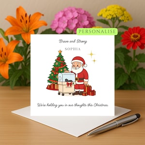 Puede incluir: Una tarjeta de Navidad con una ilustración de dibujos animados de Papá Noel con traje rojo, un árbol de Navidad decorado y cajas de regalo. La tarjeta incluye el texto "Brave and Strong" y "We're holding you in our thoughts this Christmas."