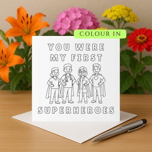 Puede incluir: Una tarjeta blanca con el texto "YOU WERE MY FIRST SUPERHEROES" e ilustraciones de cuatro figuras con capas de superhéroes. La tarjeta está rodeada de lirios naranjas, flores rosas y amarillas y una zinnia roja. Un bolígrafo plateado descansa sobre la tarjeta.
