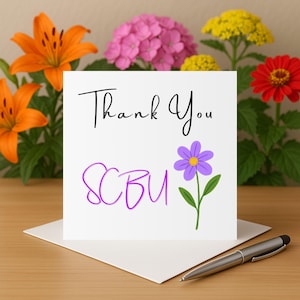 Puede incluir: Una tarjeta de felicitación blanca con las palabras "Thank You" en escritura negra y "SCBU" en escritura morada. Una flor morada con un centro amarillo también está en la tarjeta. La tarjeta está sobre un sobre blanco, con un bolígrafo plateado sobre una superficie de madera, rodeada de flores.