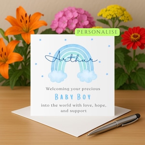 Puede incluir: Tarjeta de anuncio de nacimiento personalizada con un diseño de arcoíris en acuarela en tonos azules. La tarjeta dice "Arthur" y "BABY BOY" con el texto "Dando la bienvenida a tu precioso...al mundo con amor, esperanza y apoyo."