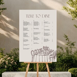 Könnte beinhalten: Ein beigefarbener Hochzeits-Sitzplan auf einer Holzstaffelei. Die Tabelle enthält eine alphabetische Liste von Namen mit den Worten "TIME TO DINE" oben. Eine Skizze eines Esstisches mit Stühlen befindet sich unten.