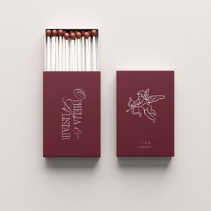 May include: Burgundy matchbox with white text "Ophelia & Alistair" and a box with matches. A second burgundy box features a Cupid illustration and the text "O&A 3 March 2017".