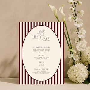 Peut inclure: Un menu de bar à rayures bordeaux et blanches avec un centre ovale. Le menu répertorie les boissons signature, le vin, la bière et les options sans alcool. Le haut du menu présente les mots "THE BAR" et une petite illustration d'un verre à cocktail avec un ange.