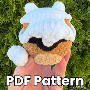May include: A crochet plush toy featuring a tan spherical body, a white textured top section, a black band across the middle, and a small white appendage on the side. The text PDF Pattern is displayed in bold white letters across the bottom section.