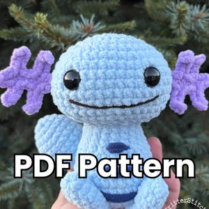 May include: A light blue crochet plushie with purple appendages and black eyes. The plushie has a smiling face and a dark blue belly. The text "PDF Pattern" is displayed in white block letters. The CritterStitch Studios logo is in the bottom right corner.