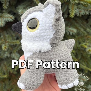Puede incluir: Un b&uacute;ho de peluche de ganchillo gris y blanco con grandes ojos amarillos y negros. El texto "PDF Pattern" se muestra en la parte delantera. El peluche tiene una textura esponjosa.