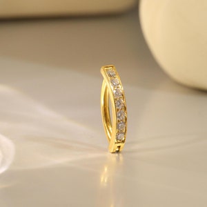 May include: A gold hoop earring with a row of clear cubic zirconia stones.