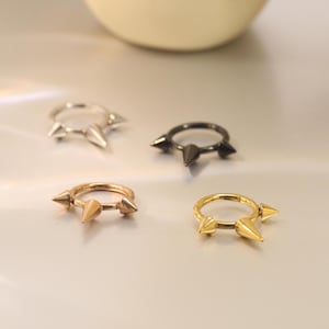 May include: Four different colored nose rings with three spikes each. The rings are silver, gold, rose gold, and black.