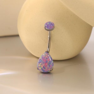 Op de afbeelding: Een navelpiercing met een gebogen, zilverkleurige staaf. De bovenste en onderste edelstenen zijn lichtpaarse opaal. De peervormige onderste edelsteen en de bovenste edelsteen hebben een mix van roze, paarse en iriserende kleuren.