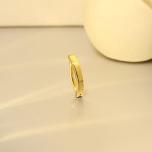 Puede incluir: Un anillo dorado con un diseño curvo. El anillo tiene una superficie lisa y pulida y una estética minimalista. El anillo probablemente está hecho de metal y está diseñado para usarse en un dedo.