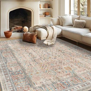 May include: A large, rectangular area rug with a detailed, vintage-inspired design. The rug features a cream-colored base with intricate patterns in shades of red, blue, and beige. The rug is placed in a living room setting with a fireplace and a sectional sofa.