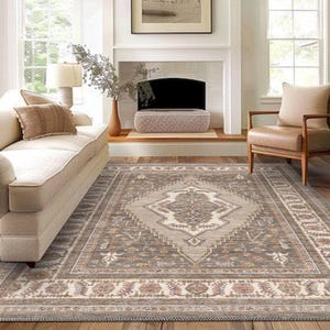 May include: A large, rectangular area rug with a central diamond pattern in shades of gray, beige, and brown. The rug features a detailed border and is placed on a hardwood floor in a living room setting.