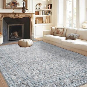 May include: A light gray area rug with a blue and white patterned design. The rug is in a living room with a white couch and a fireplace.