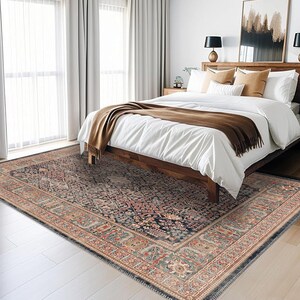 May include: A rectangular area rug with an intricate, traditional pattern in navy blue, red, and beige tones. The rug is placed on a white wooden floor in a bedroom setting, with a bed and curtains visible in the background.