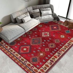 Op de afbeelding: Een rood, beige en blauw tapijt met een geometrisch ontwerp. Het tapijt heeft een crèmekleurige rand met een herhalend patroon van gestileerde bloemen.