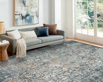 Könnte beinhalten: Ein Wohnzimmer mit einem grauen Sofa, Kissen und einem gemusterten Teppich. Der Teppich hat ein verwittertes, Vintage-Aussehen mit blauen, beigen und weißen Blumenmustern. Ein abstraktes Gemälde hängt an der Wand.