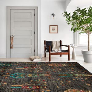 K&ouml;nnte beinhalten: Ein dunkelgrauer Teppich mit einem bunten Blumenmuster mit B&auml;umen und Blumen. Der Teppich befindet sich in einem Raum mit einem Holzstuhl, einer Topfpflanze und einer T&uuml;r.
