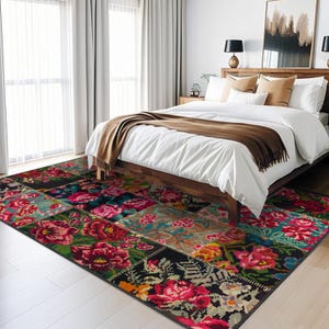 May include: A colourful floral patterned rug with a patchwork design in shades of red, pink, green, blue, and black. The rug is placed in a bedroom with a white bed and brown blanket.