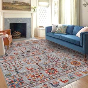 Puede incluir: Una alfombra gris con un patrón geométrico colorido que presenta árboles, flores y otros diseños abstractos. La alfombra está colocada en una sala de estar con un sofá azul y una chimenea.