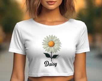 以下が含まれることがあります： 白いクロップトップに、デイジーの花のグラフィックと黒い文字で「Daisy」とプリントされています。