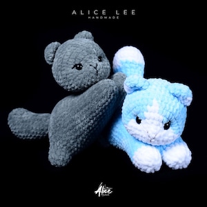 Puede incluir: Dos peluches de gato hechos a mano con ganchillo. Uno es gris, el otro azul claro con detalles blancos. Ambos tienen ojos negros y están sobre un fondo negro. El texto "ALICE LEE HANDMADE" y "Alice" son visibles.