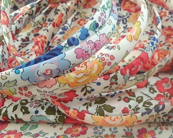 May include: A close-up of several rolls of white fabric with a floral print in shades of pink, blue, yellow, and red. The fabric is folded and layered, creating a textured effect.