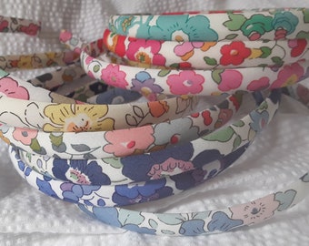 May include: A stack of eight floral patterned headbands in various colors, including blue, pink, and yellow. The headbands are made of fabric and have a simple design.