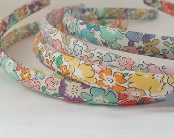 May include: Three floral patterned headbands in shades of pink, yellow, green, and blue. The headbands are made of fabric and are designed with a white background.