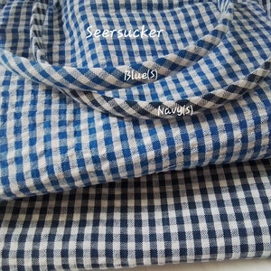 May include: Two pieces of blue and white checkered seersucker fabric. The top piece is a lighter blue and the bottom piece is a darker navy blue. The text "Seersucker", "Blue (S)", and "Navy (S)" is visible on the fabric.