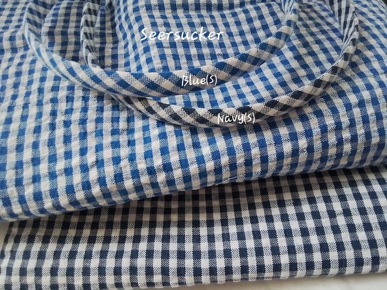 May include: Two pieces of blue and white checkered seersucker fabric. The top piece is a lighter blue and the bottom piece is a darker navy blue. The text "Seersucker", "Blue (S)", and "Navy (S)" is visible on the fabric.