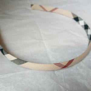 May include: A beige, black and red patterned headband. The headband is made of a soft, stretchy material.