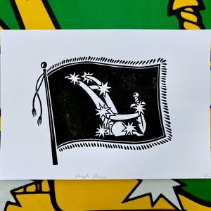 May include: A black and white print depicting a flag with a distinctive design. The flag has a black field with white stars and a sword. The print is on a white background.