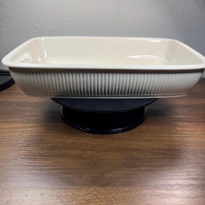 May include: A rectangular off-white ceramic baking dish featuring a ribbed exterior pattern and a beaded rim detail along the top edge. The dish has a smooth interior surface and a deep basin, designed for oven use with a clean, uniform finish.