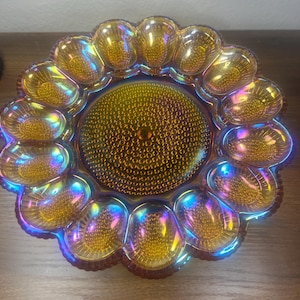 May include: An iridescent amber glass serving dish with a sunflower design. The dish features a central circular area surrounded by petal-shaped compartments. The glass has a textured surface and reflects a rainbow of colors.