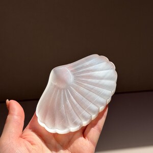 以下が含まれることがあります： 半透明のつや消しホワイトの貝殻型オブジェで、扇状の畝のある質感が特徴です。滑らかな曲線を描く縁と、光を反射して表面の放射状の隆起を際立たせる半透明の仕上げが施されています。