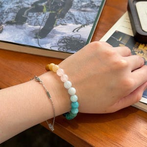 May include: A colorful beaded bracelet with a gradient of yellow, pink, light blue, and turquoise beads. The bracelet is on a person's wrist.