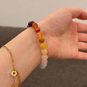 May include: A rainbow colored beaded bracelet with round, smooth stones. The bracelet is worn on a person's wrist.