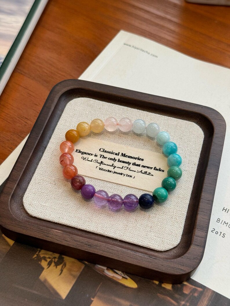 May include: A rainbow colored gemstone bracelet with a wooden box. The bracelet is made of various gemstones, including amethyst, turquoise, and lapis lazuli. The box is made of dark wood and has a light brown fabric lining. The text on the box reads: "Classical Memories Elegance is The only beauty that never fades Hand Craftsmanship and Home Authitics Wooden jewelry box"