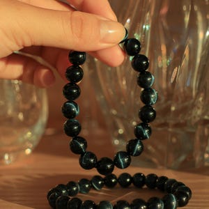 May include: Two blue tiger's eye beaded bracelets. The bracelets are made of dark blue beads with a light blue iridescent sheen.