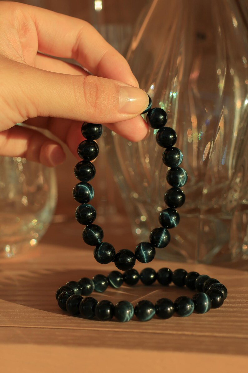 May include: Two blue tiger's eye beaded bracelets. The bracelets are made of dark blue beads with a light blue iridescent sheen.