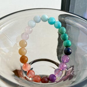 May include: A rainbow gemstone bracelet with beads in shades of pink, orange, red, green, blue, and purple.