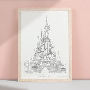 May include: A framed black and white line drawing of a detailed castle with multiple towers and spires. The artwork is in a light wood frame and is displayed against a pink background. The text at the bottom reads "LE CHATEAU DE LA BELLE AU BOIS DORMANT".