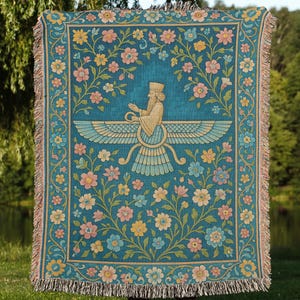 May include: Teal throw blanket with a floral and mythological design. The blanket features a central figure with outstretched wings, surrounded by colorful flowers. The edges have a fringed trim. The blanket is held up in front of a person.