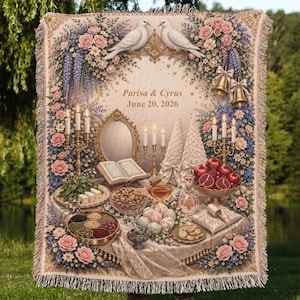 May include: A woven throw blanket featuring a detailed illustration of a Haft-Sin table with pomegranates, candles, a mirror, and an open book. The text reads Parisa & Cyrus June 20, 2026, framed by white doves, pink roses, and blue flowers with fringe edges.