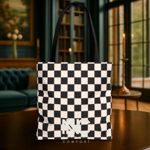 May include: A black and white checkered tote bag with black handles. The bag features the text "NC" and "NUANCED COMFORT" in white. The bag is made of a sturdy material and is suitable for carrying various items.