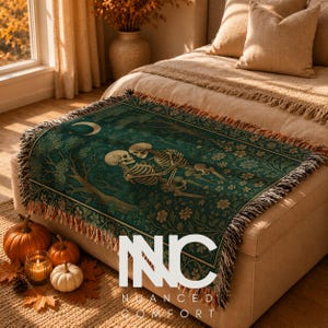 May include: A woven throw blanket featuring a dark green background with a central illustration of two skeletons embracing in a forest under a crescent moon, surrounded by floral patterns and finished with a fringed edge, labeled with the text NUANCE COMFORT.