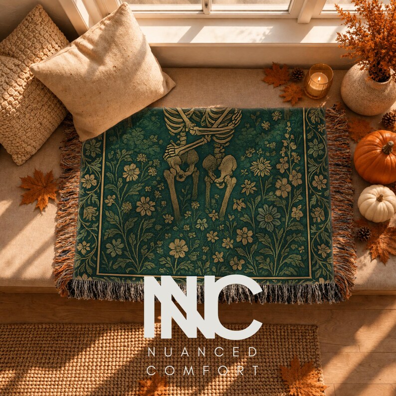 May include: A rectangular woven throw blanket featuring a dark teal background with a repeating pattern of cream-colored skeletons and floral botanical illustrations. The blanket has a fringed edge and displays the text NUANCED COMFORT in white.