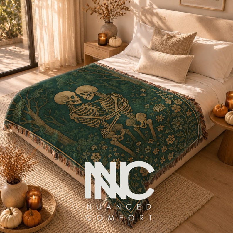 May include: A dark green woven throw blanket featuring a graphic illustration of two skeletons embracing amidst a forest of trees and flowers. The blanket has a fringed edge and is draped over a bed with white bedding and beige pillows.